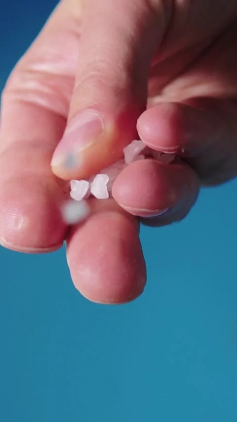 Vertical macro shot of hand dropping pink salt crystals on blue background Stock Footage 346639633