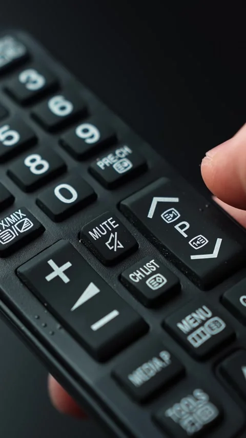 Vertical macro shot of a hand pressing the mute button on a TV remote, showing Stock Footage 331318374