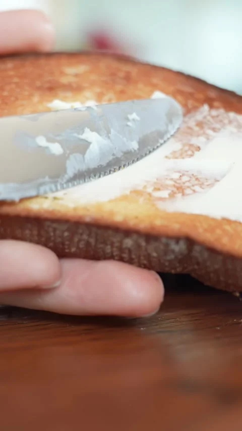 Vertical macro shot of a knife spreading creamy topping on toasted bread Stock Footage 333650362