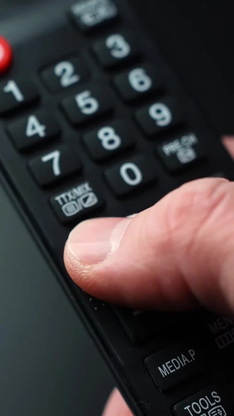 Vertical macro shot of a thumb pressing the volume up button on a TV remote Stock Footage 329470372