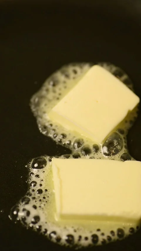 Vertical macro of two butter pieces melting on a hot frying pan 库存影片 344890637