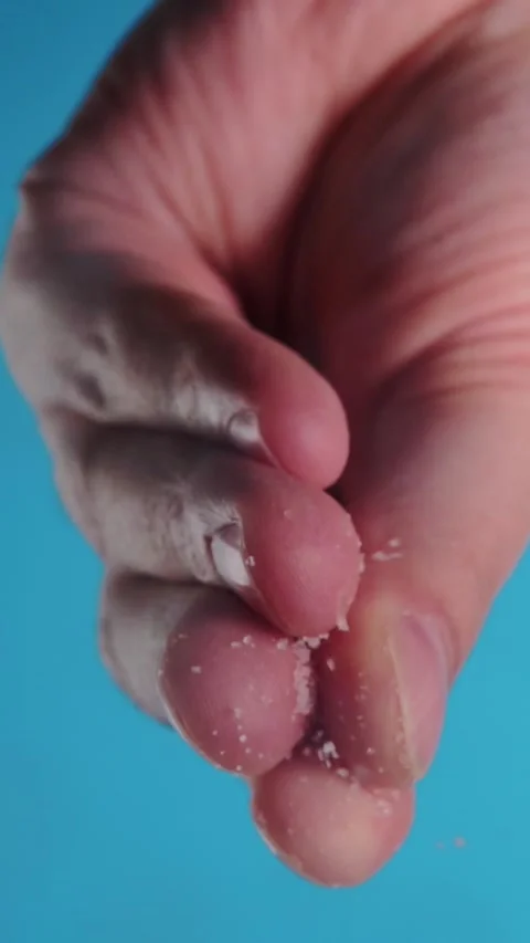 Vertical macro view of hand sprinkling fine white salt on blue background Stock Footage 346639629
