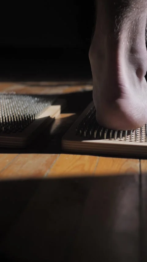 Vertical: Male bare feet step on sharp nails of a Sadhu indoors on a wooden parq Stock Footage 267019458