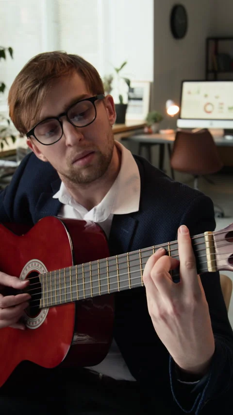 Vertical of Male Employee Learning to Play Guitar during Workday in Empty Office Stock Footage 331533353