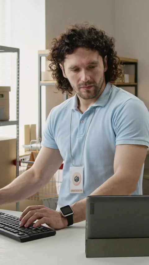 Vertical of Male Warehouse Worker Typing on Computer in Fulfillment Center Stock Footage 346054418
