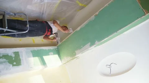 Vertical. a man in overalls applies plaster with a spatula to the wall Stock Footage 145492257