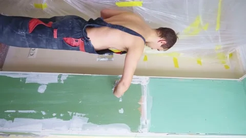 Vertical. a man in overalls applies plaster with a spatula to the wall Stock Footage 145754913