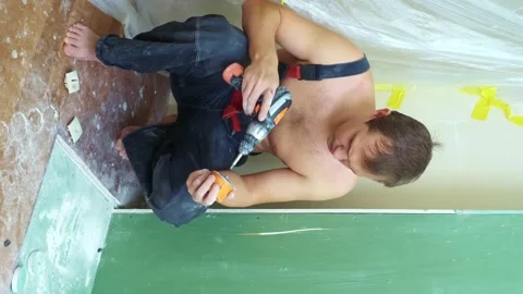 Vertical. a man in overalls inserts a socket into the wall with a screwdriver Stock Footage 147070367