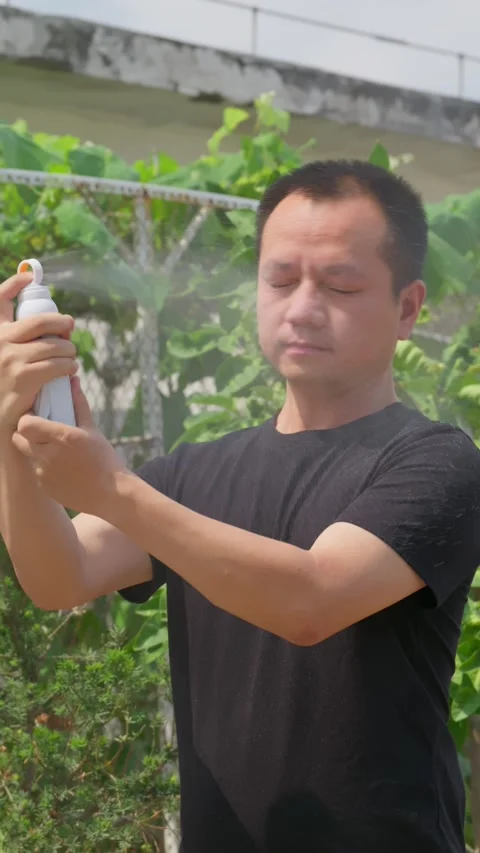 Vertical man sprays sunscreen on his face to prevent sunburn in hot summer. 動画素材 336038021