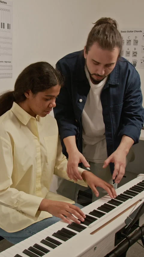 Vertical of Man Teaching Female Student Playing Piano in Music Studio Stock Footage 339187776