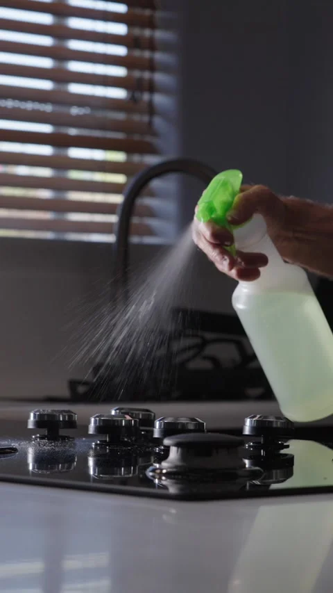 Vertical man using spray bottle to spray soapy water on stove top to clean Stock Footage 284244155