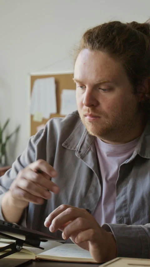 Vertical of Man Working on Laptop While Writing Notes in Office Stock Footage 348141263