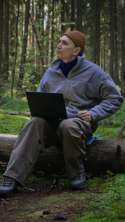 Vertical of Man Working Remotely on Laptop Sitting on Log in Pine Forest Stock Footage 348053850