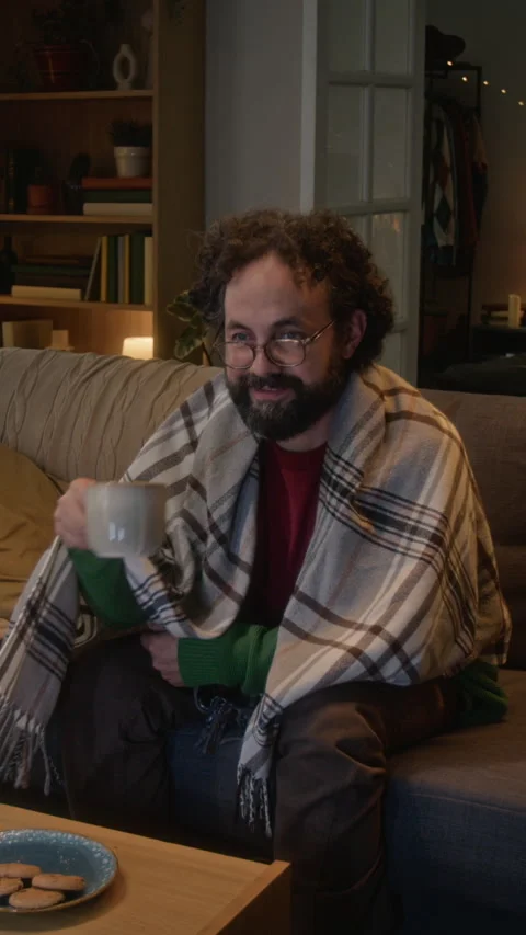 Vertical of Man Wrapped in Blanket Watching Tv Drinking Coffee at Home Stock Footage 341675465