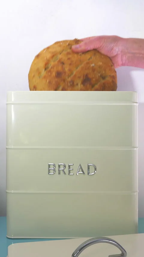 Vertical - A man’s hand placing an uncut loaf into a painted metal bread bin. Stock Footage 280229419