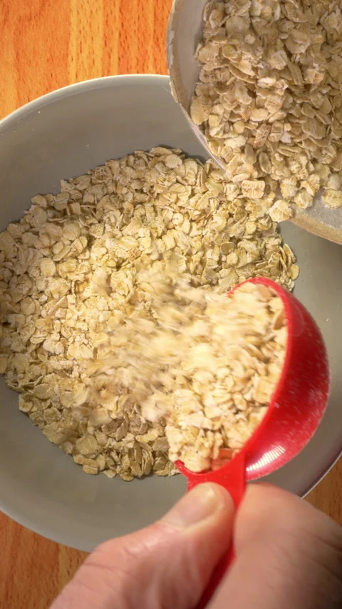Vertical - Man’s hand scooping dry porridge oats from a container into a bowl. Vídeos de archivo 301544944