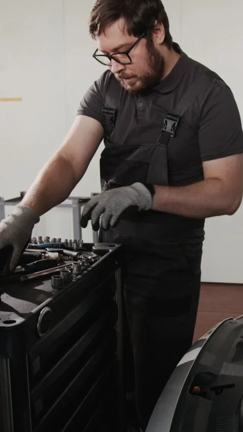 Vertical of Mechanic Repairing Car Engine and Apprentice Bringing Tool Cart Stock Footage 329439989