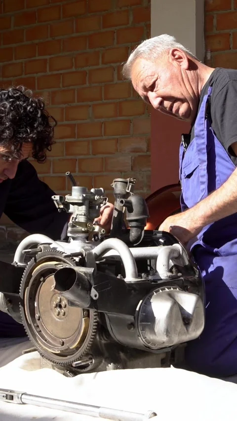 Vertical Mechanics collaborating to repair a motor in a sunny garage setting Stock Footage 313230071