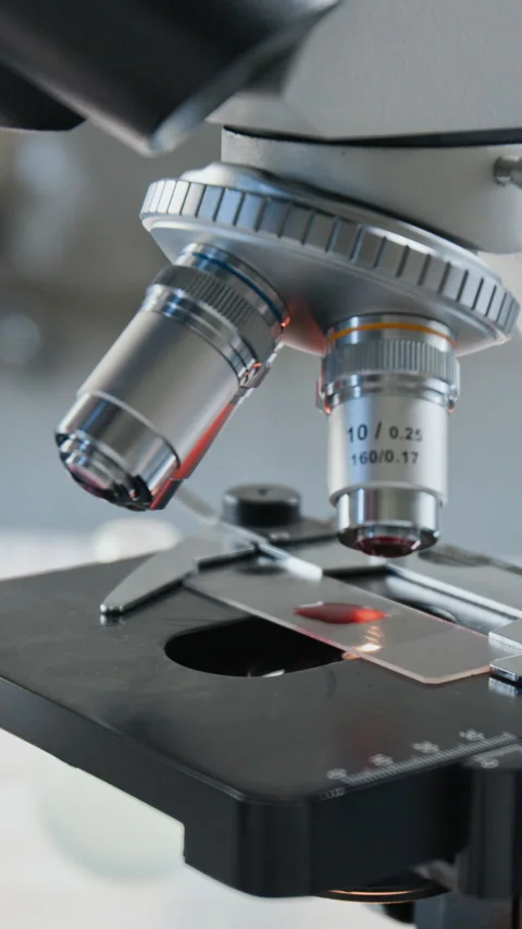 Vertical of Microscope Examining Blood Sample on Glass Slide in Laboratory Stock Footage 347048854