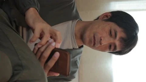 Vertical : Middle aged asian man using his smartphone at home. 25P. Stock Footage 224898332