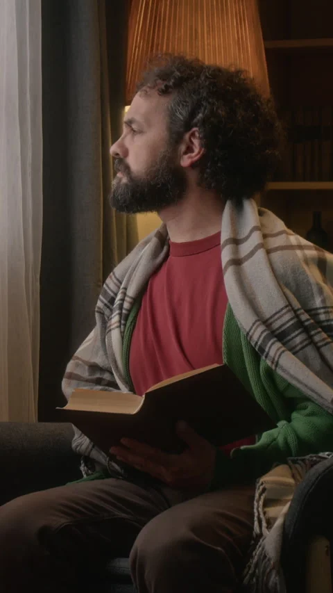 Vertical of Middle Aged Man Reading Book and Looking Thoughtfully out Window Stock Footage 341675459