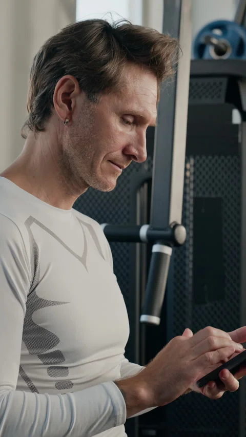 Vertical of Middle Aged Man Using Fitness App on Smartphone in Gym Stock Footage 345199842