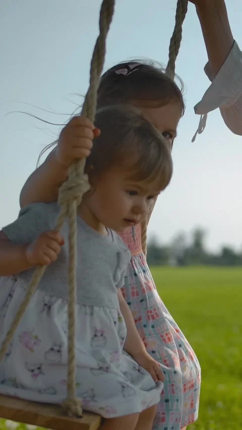 Vertical of Mom shakes two small sisters, 1 and 3 years old, on a wooden swing Stock Footage 276932095