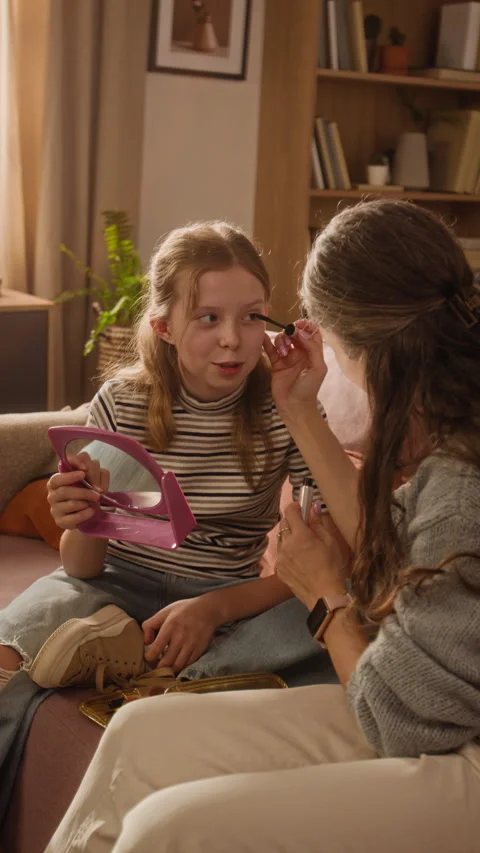 Vertical of Mother Teaching Daughter How to Use Lash Cosmetics in Living Room Stock Footage 334337177