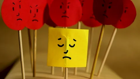 Vertical motion closeup of yellow paper with sad face surrounded by angry f.. Stock Footage 291647534