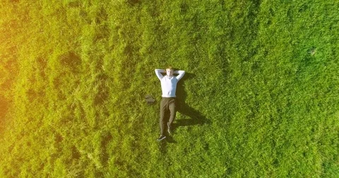 Vertical motion flight over businessman lying on fresh green meadow. Top view on Stock Footage