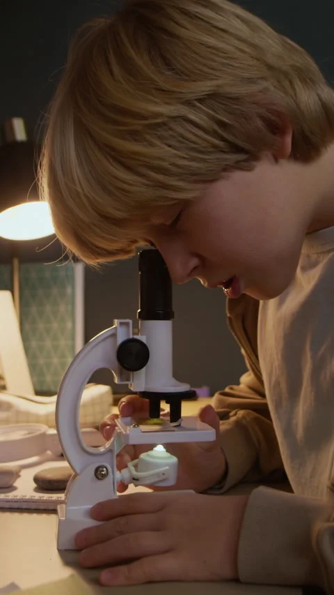 Vertical of Motivated Boy Child Using Microscope at Home Desk Stock Footage 326664508