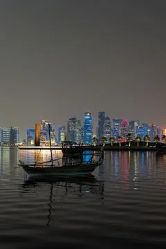 Vertical night view of illuminated Doha skyline, traditional dhow boats. Stock Photos
