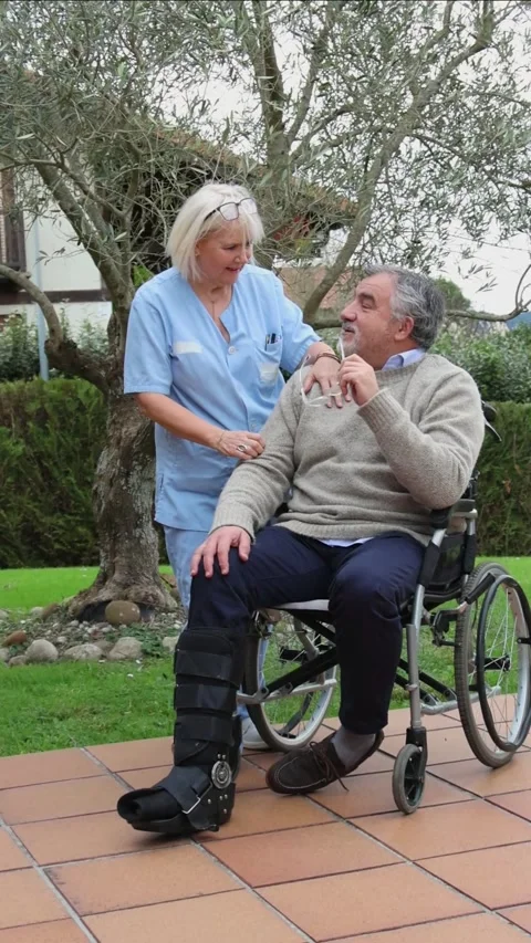 Vertical Nurse assisting elderly man in wheelchair in a garden Stock Footage 300172227