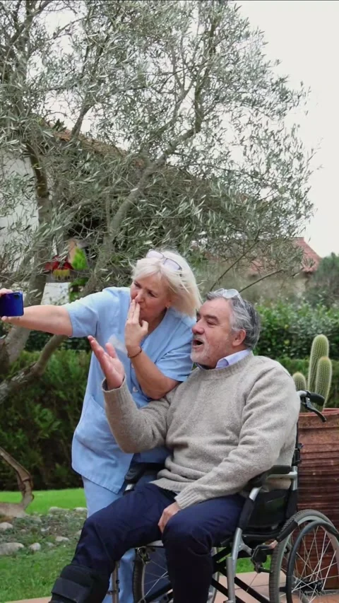 Vertical Nurse taking selfie with elderly patient in wheelchair sending kisse Stock Footage 300172233