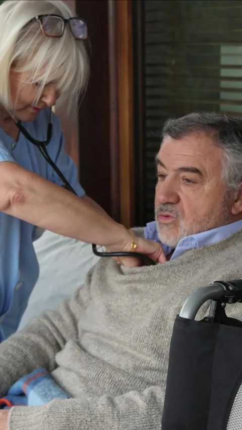 Vertical Nurse using stethoscope examining senior man in wheelchair Stock Footage 300172223