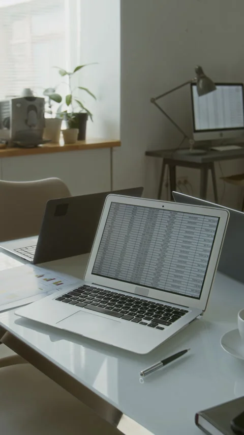 Vertical of Office Workspace with Laptop Displaying Spreadsheet on White Table Stock Footage 312059018