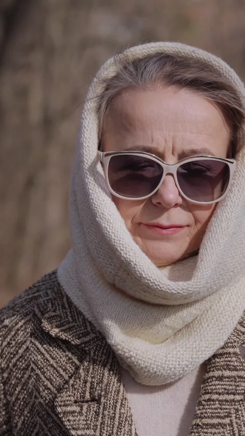 Vertical. Old lady wearing warm scarf and large sunglasses walks across park Video stock 329637011