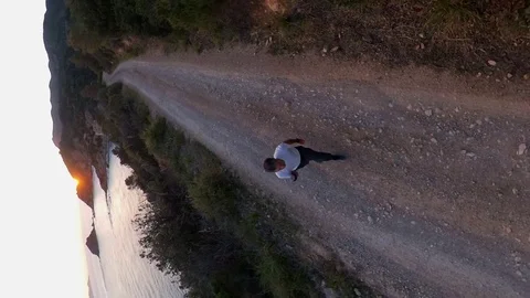 Vertical, orbit around a man walking on a scenic path on the cliff at sunset Stock Footage 107921074