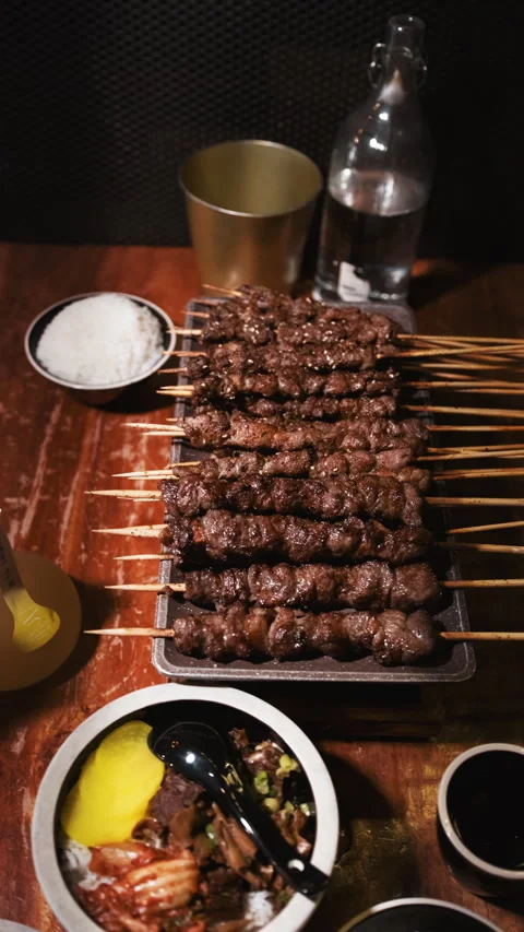 Vertical overhead view of grilled meat skewers and Asian side dishes on table Stock-Footage 333878856