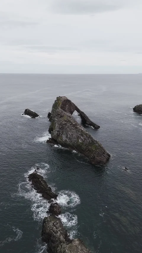 Vertical pan drone shot of Bow Fiddle Rock rising above the Scottish coastline Stock Footage 334951058