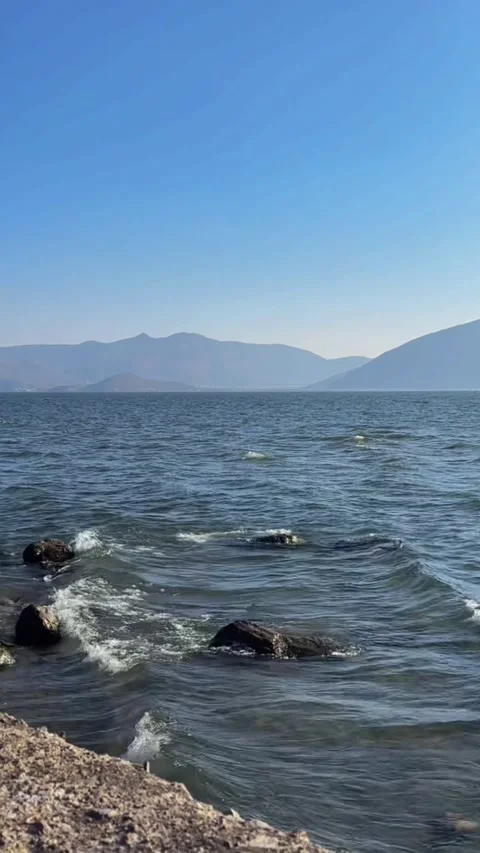 Vertical panning shot of crystal clear waves on Erhai Lake with blue mountai Stock-Footage 328791095