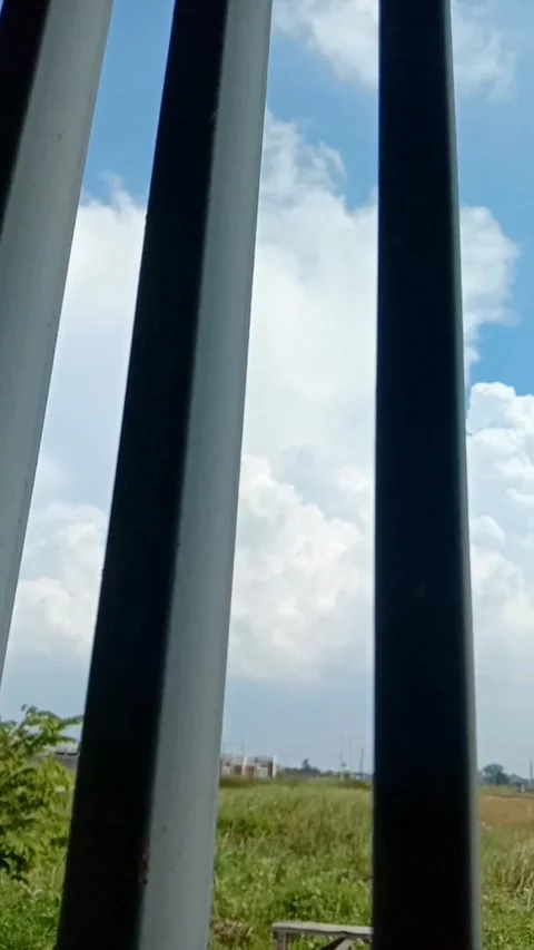 Vertical panning shot right of blue sky and landscape behind fence bars Stock-Footage 333484848
