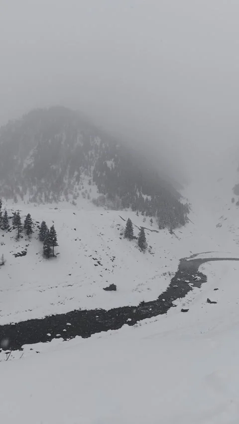 Vertical Panning Shot of Winding River and Misty Mountain in Heavy Snow Video stock 327690525