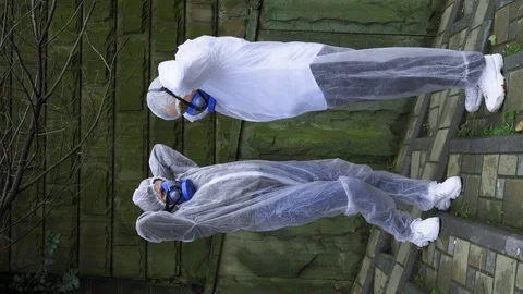 Vertical, people in protective suits and respirators in the city Park talking Stock Footage 124987024