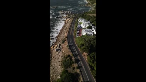 Vertical perspective captures a snaking road tracing the rugged coast of Camps Stock Footage 270613966