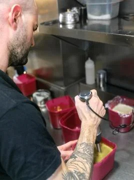 Vertical photo of a cook using a mixer to remove sauce in a plastic container in Stock Photos