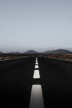 Vertical photo empty road stretches towards distant mountains under a calm sky Stock Photos