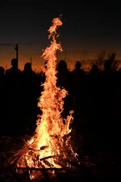 Vertical photo. towering flame flickers in night as crowd stand, Stock Photos