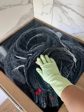 Vertical photo of a womans hand in a rubber glove cleaning an electric stove Foto stock