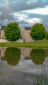 Vertical Pond with reflection of multi storey homes lush trees and cloud filled Stock Photos